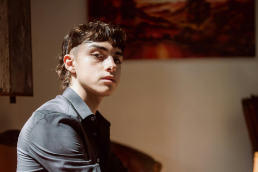 Young man with a modern mullet haircut sitting indoors in natural light.